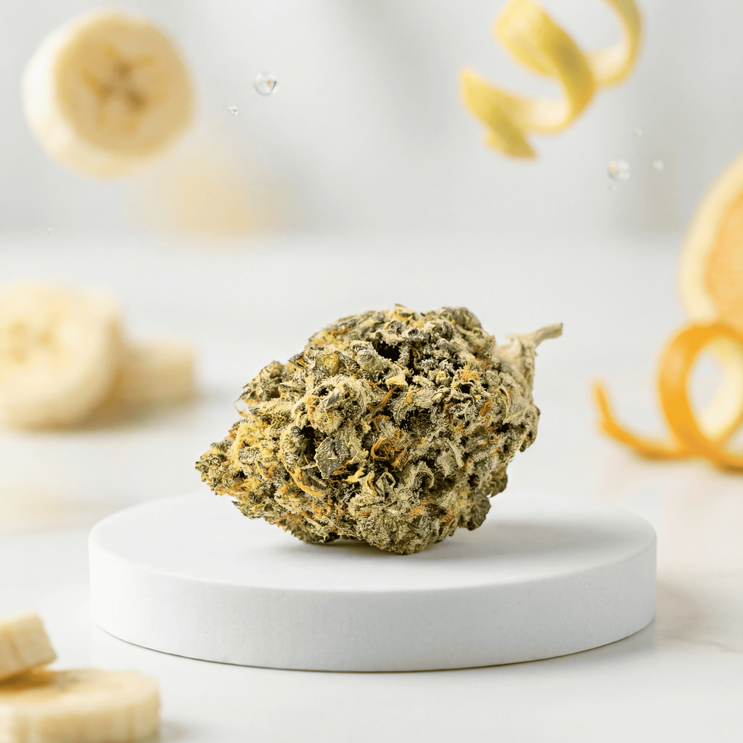 Banana Sour Verpackung mit CBD Blüte auf weißem Podest und Banane im Hintergrund